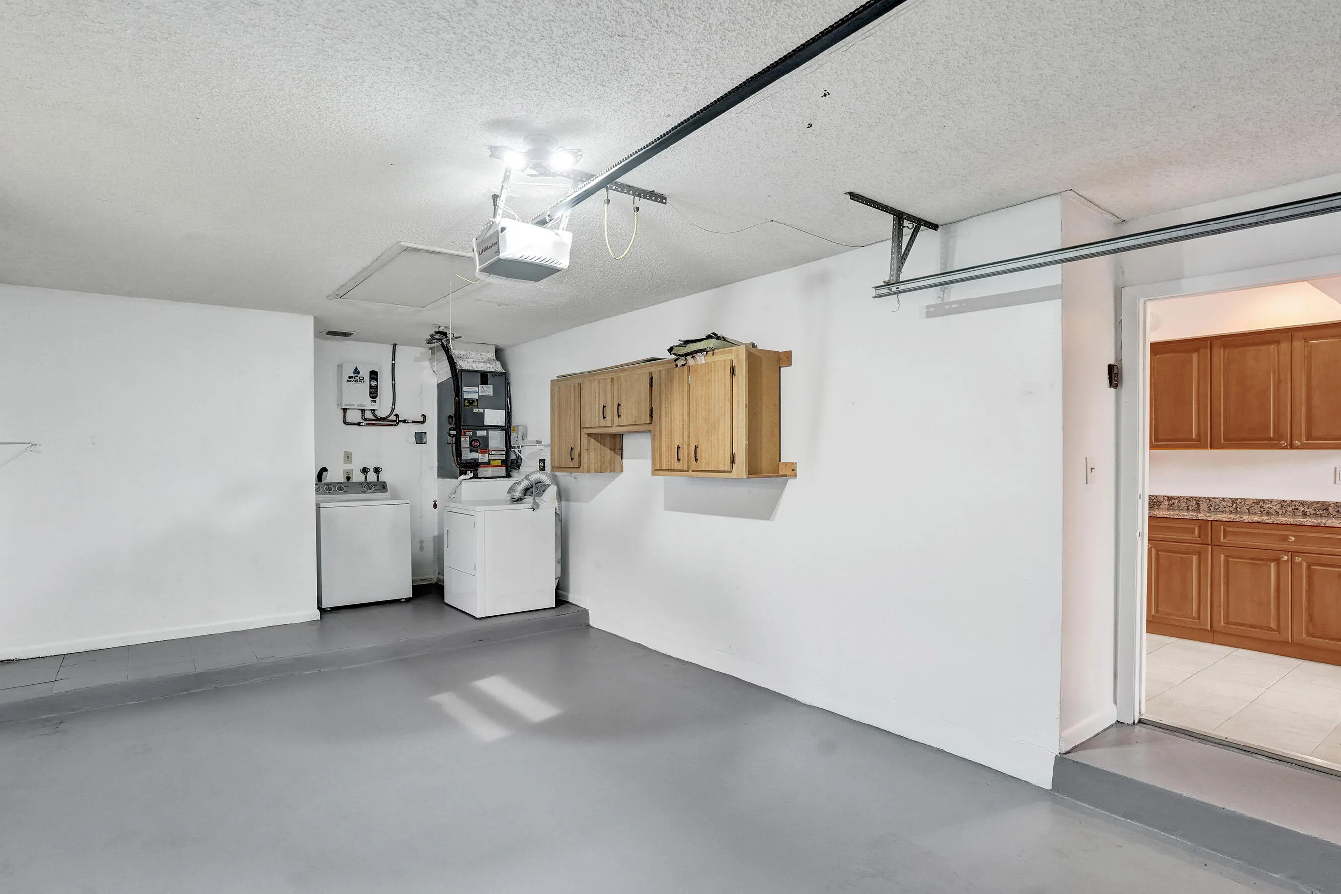 Spacious garage with light wood-finish cabinetry, a utility sink, and laundry appliances