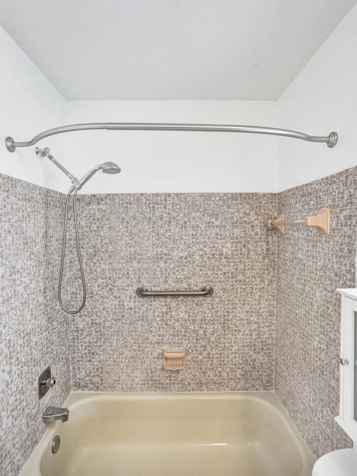 Bathtub with mosaic tile surround, curved shower rod, and integrated grab bar