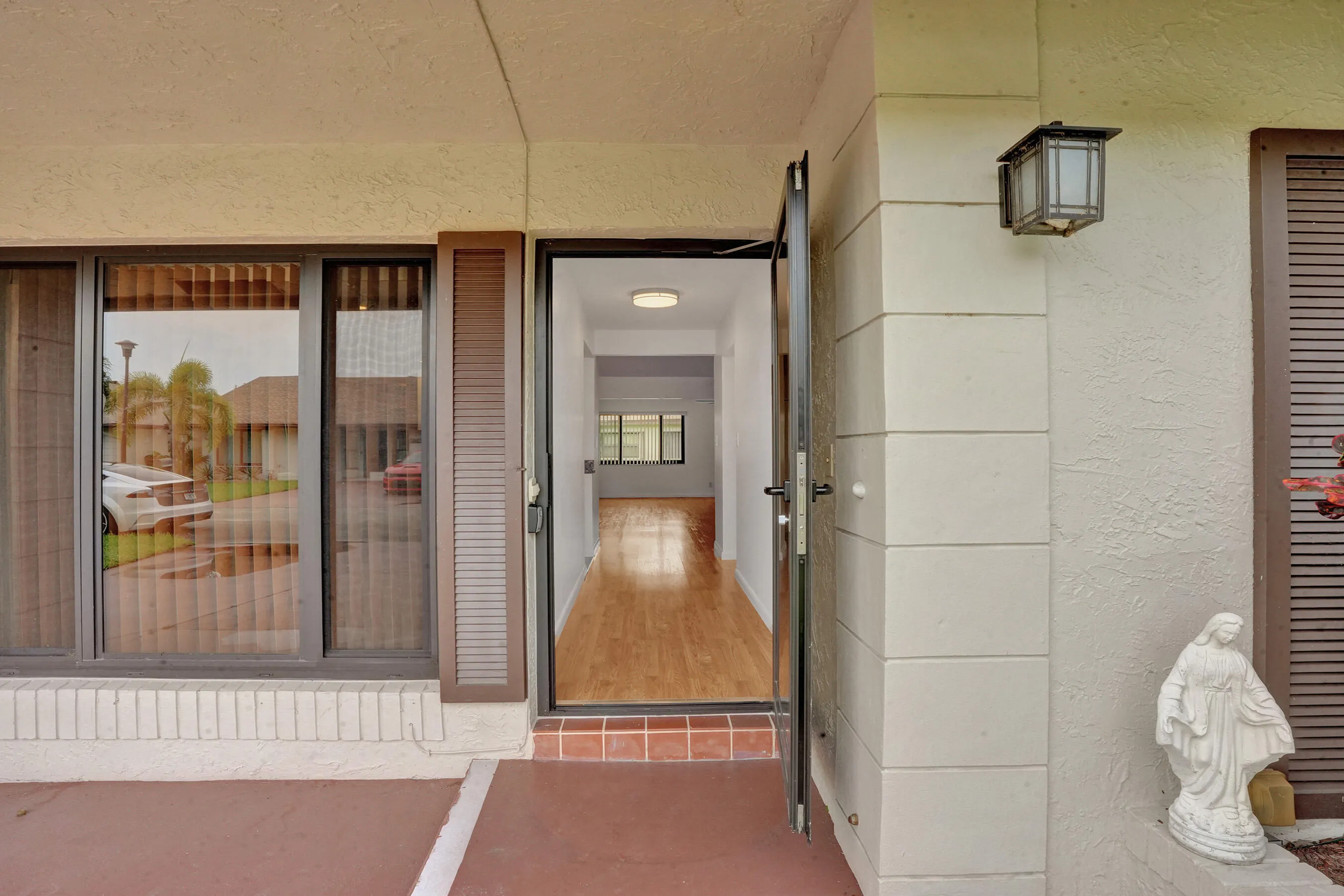 Covered entry with exterior wall sconce, full-light entry door, sidelight window, and wood-finish flooring