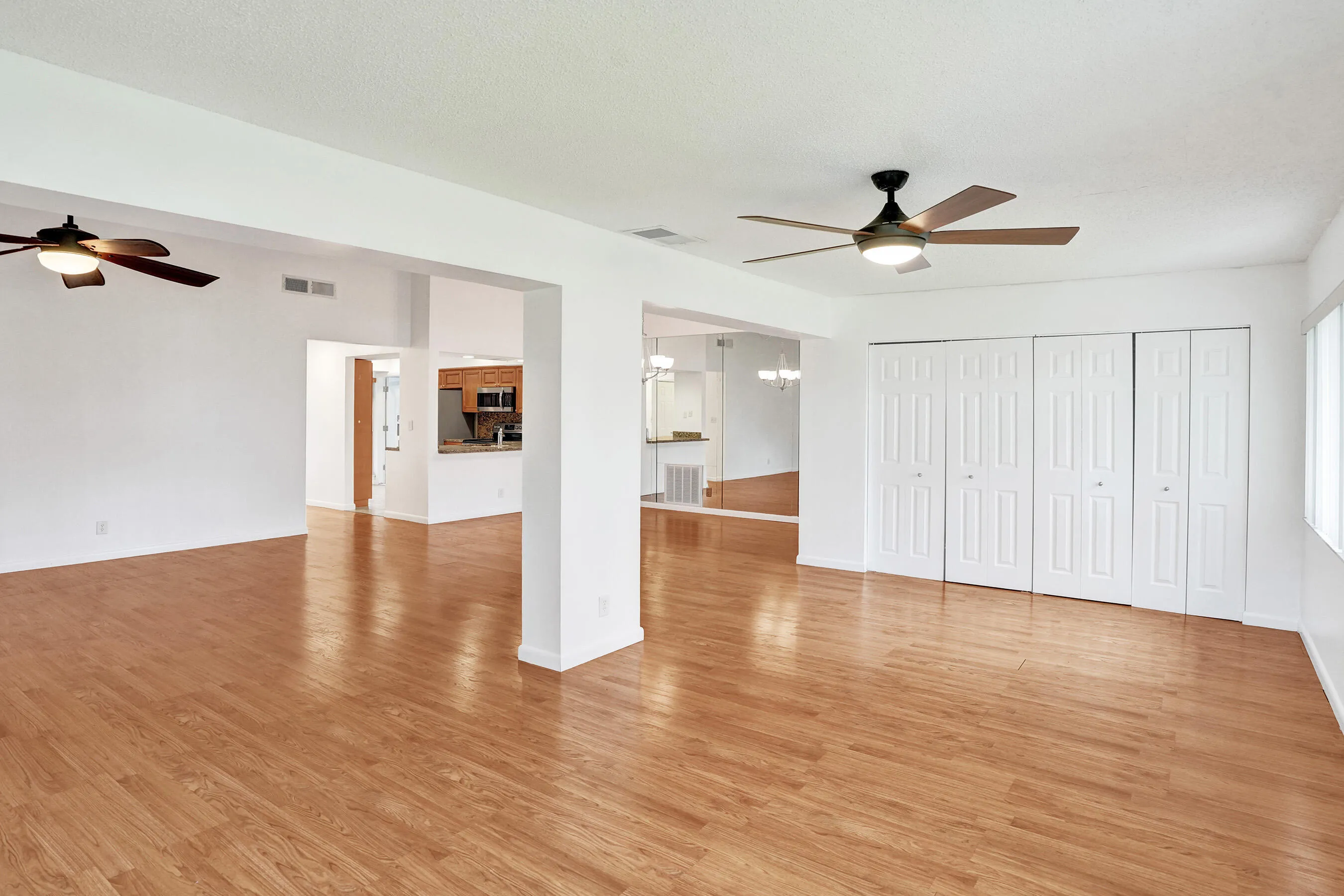 Wood-finish flooring, white walls, two ceiling fans with integrated lighting, and bi-fold closet doors