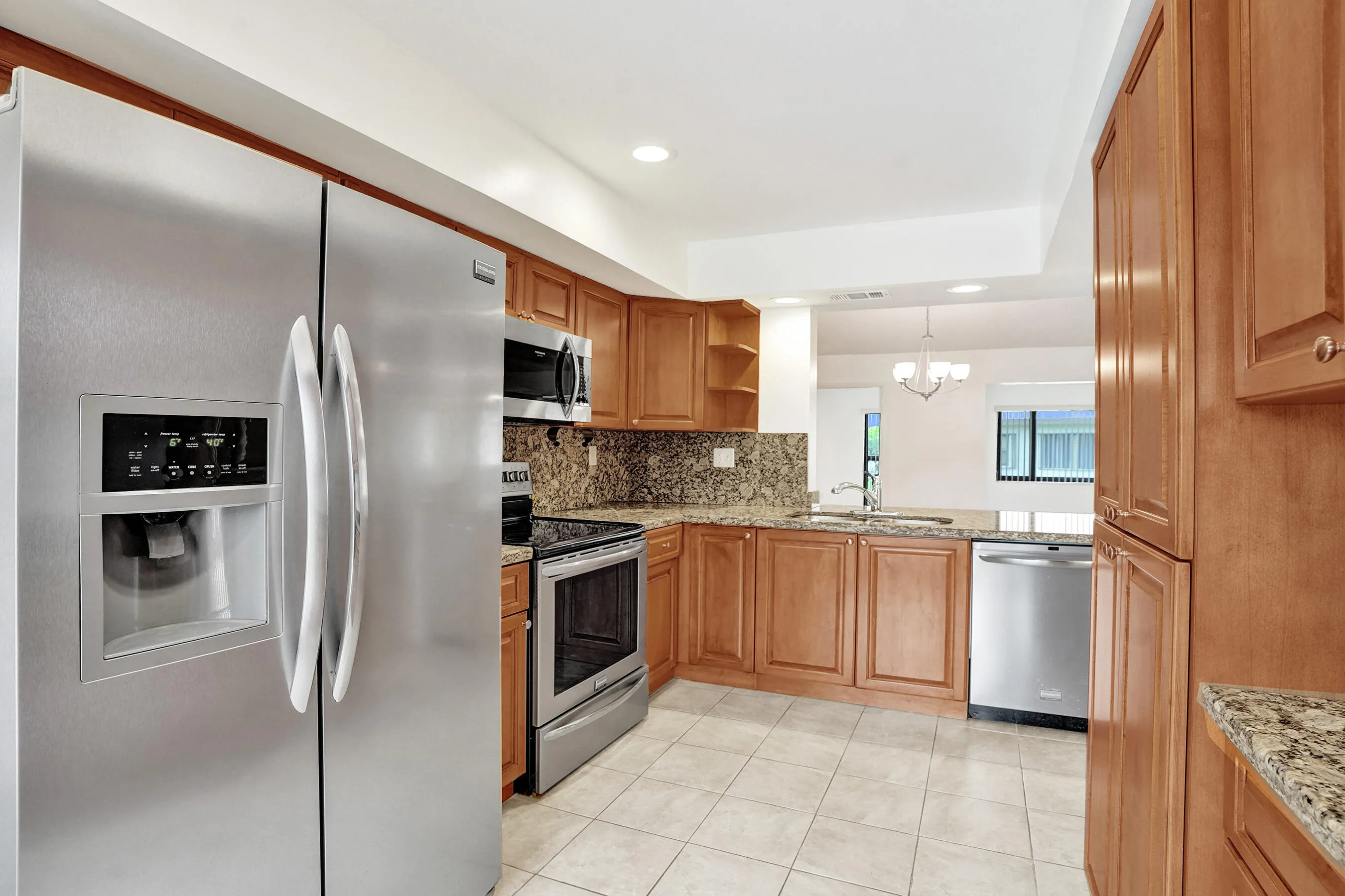 Kitchen featuring stainless steel appliances, wood cabinetry, granite countertops, and tile flooring