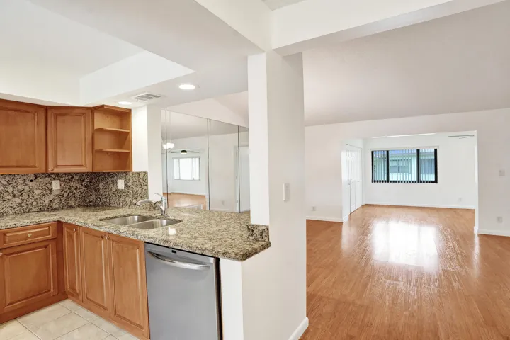 Kitchen featuring wood cabinetry, stone countertops, double basin sink, and stainless steel dishwasher