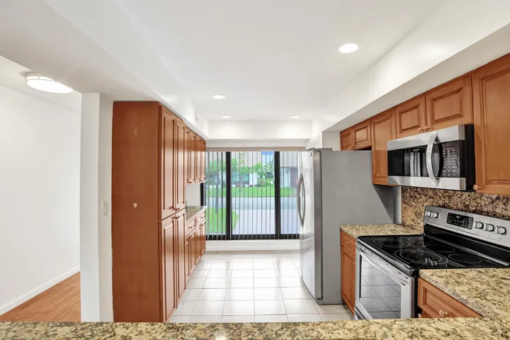 Kitchen featuring wood cabinetry, stainless steel appliances, tiled flooring, granite countertops, and recessed lighting