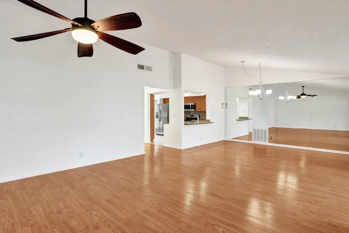Spacious living area featuring wood-finish flooring, a ceiling fan with integrated lighting, and mirrored wall accents