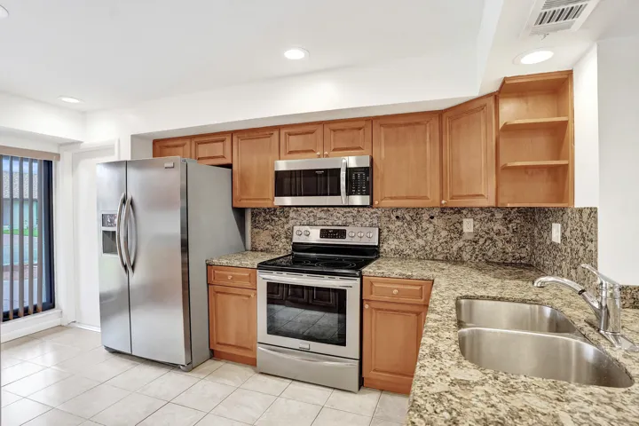 Kitchen featuring stainless steel appliances, wood cabinetry, granite countertops, and a double basin sink