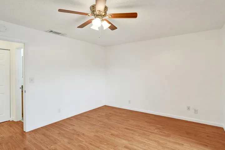 Wood-finish flooring, ceiling fan with integrated lighting, and a white interior door