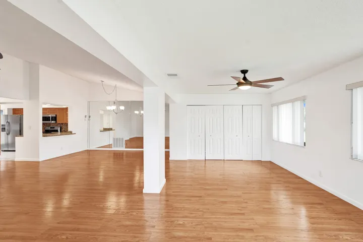 Expansive open-concept living area featuring wood-finish flooring, two windows with blinds, and a ceiling fan