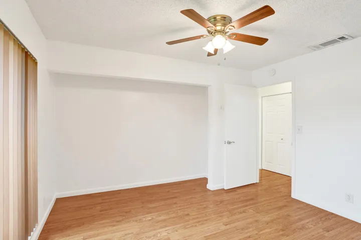Wood-finish flooring, ceiling fan with integrated lighting, and a white interior door