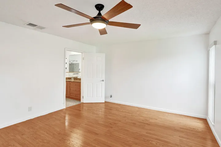 Wood-finish flooring with white baseboards, a ceiling fan with integrated lighting, and a white paneled door