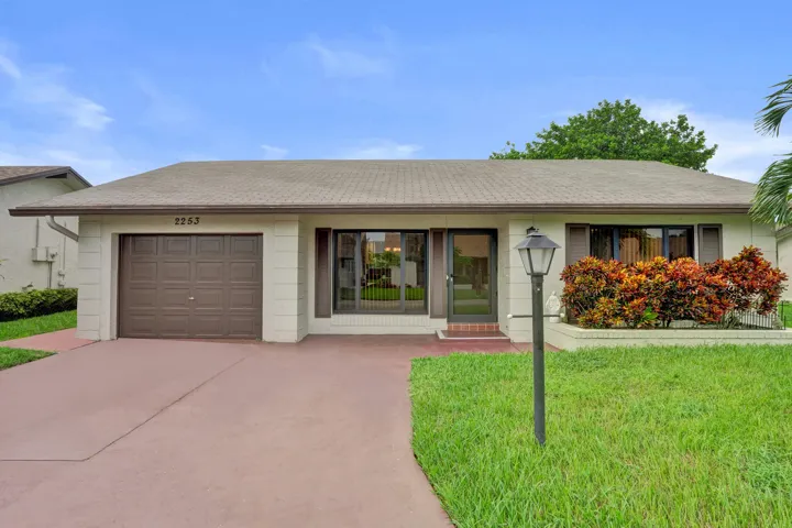 Single-story residence featuring a brown garage door, front entry, landscaped shrubbery, and a paved driveway