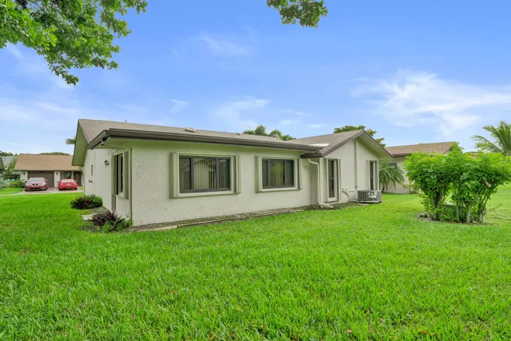 Expansive lawn space surrounding the property, featuring a stucco exterior, brown shingle roof, and multiple windows