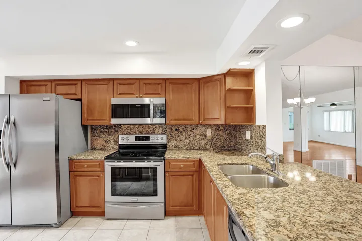 Kitchen featuring wood cabinetry, stainless steel appliances, speckled stone countertops, and a double basin sink