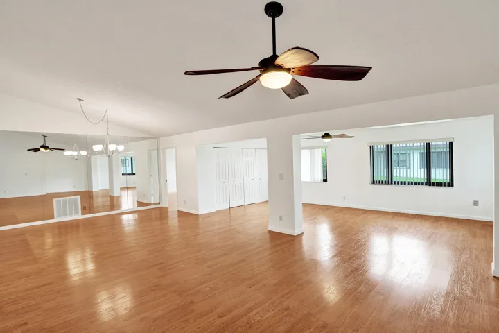Vaulted ceiling with a ceiling fan, wood-finish flooring, mirrored wall, built-in storage, and multiple windows