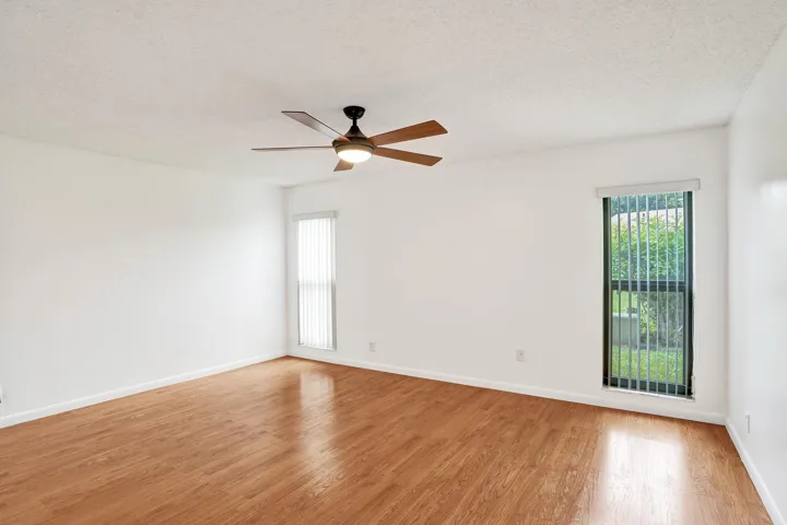 Spacious room featuring wood-finish flooring, white walls, and a ceiling fan with integrated lighting