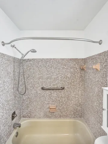 Bathtub with mosaic tile surround, curved shower rod, and integrated grab bar