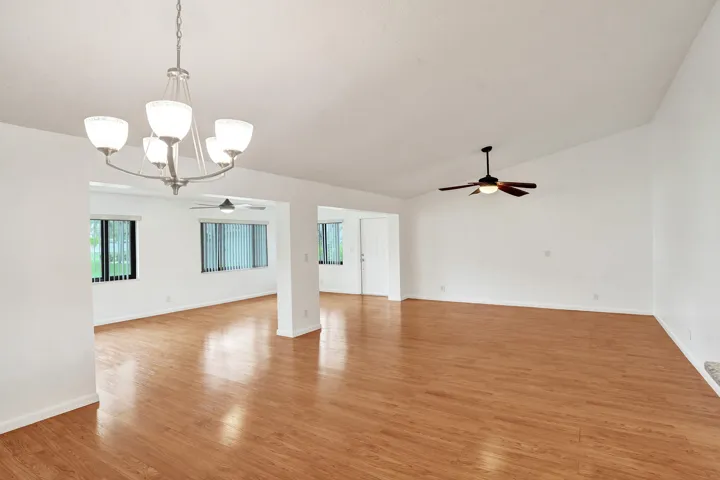 Vaulted ceiling with a ceiling fan, wood-finish flooring, recessed lighting, and multiple windows with vertical blinds