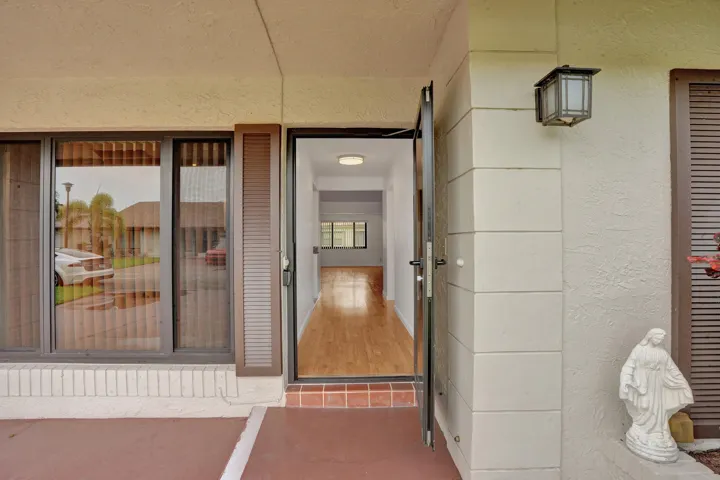 Covered entry with exterior wall sconce, full-light entry door, sidelight window, and wood-finish flooring