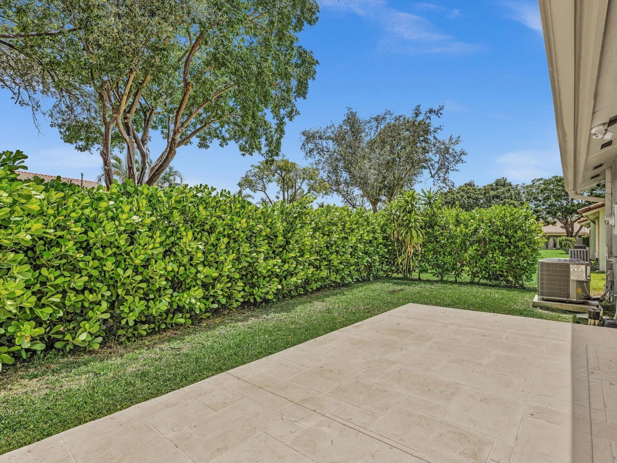 Expansive patio with stone-finish pavers, surrounded by lush green lawn and mature privacy hedges