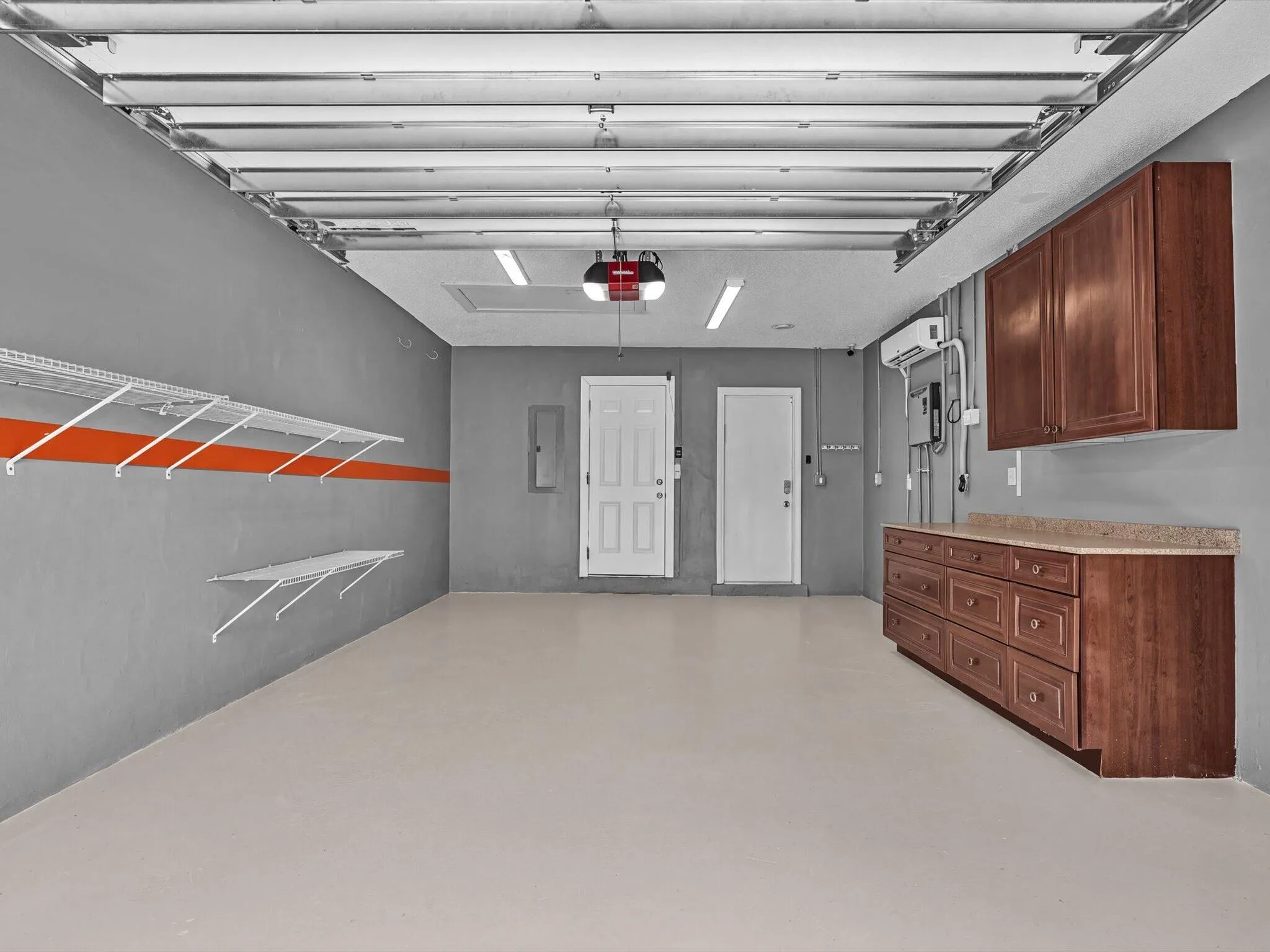 Spacious garage with epoxy flooring, built-in cabinetry with a stone-finish countertop, wall-mounted shelving, and overhead fluorescent lighting