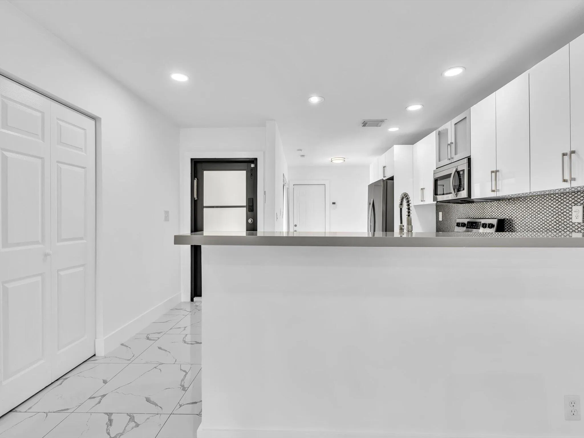Contemporary kitchen with white cabinetry, stainless steel appliances, a mosaic tile backsplash, and a breakfast bar