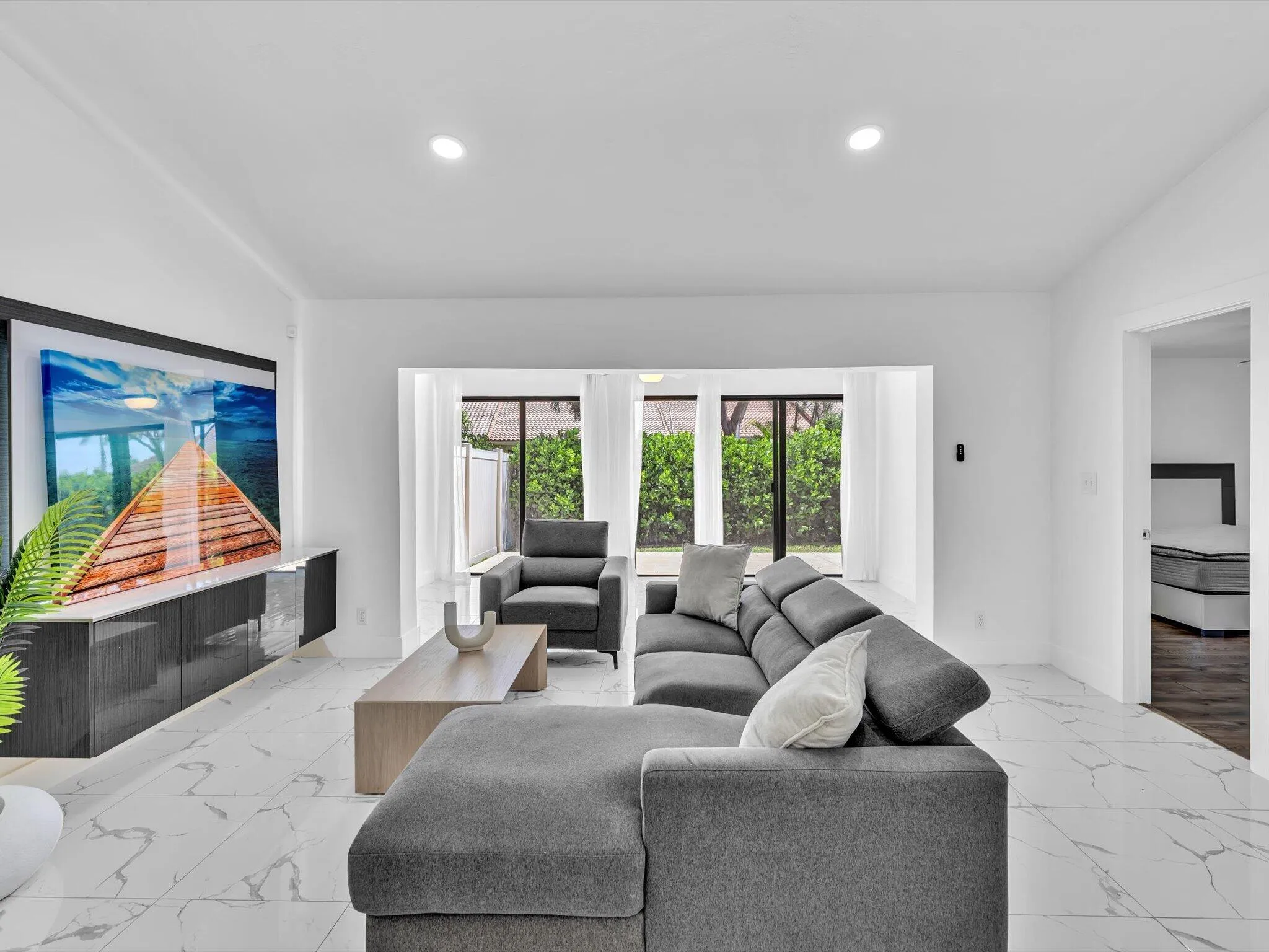 Recessed lighting, large format tile flooring, black frame glass doors, white wall finishes, and a built-in media console