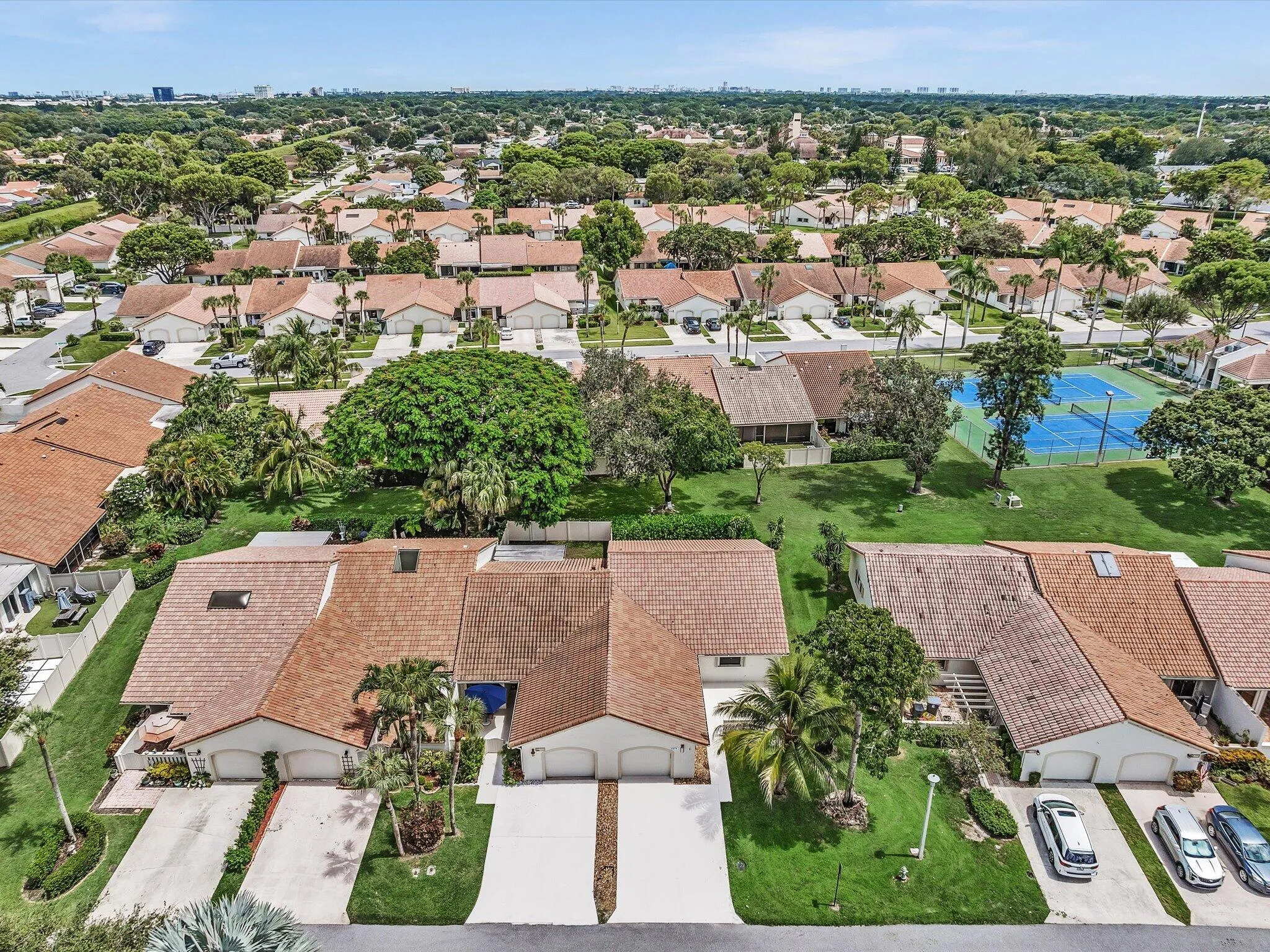 Aerial perspective showcasing a residential community with mature landscaping, multiple properties with tiled roofs, and a tennis court