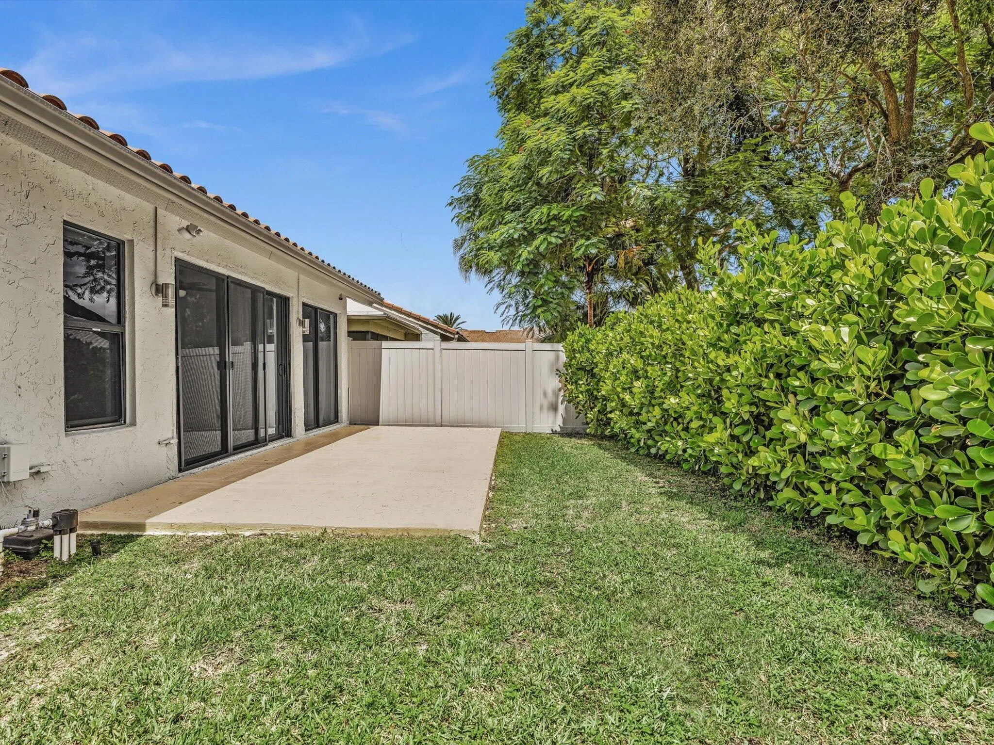 Private backyard with a concrete patio, lush green lawn, and mature privacy hedging