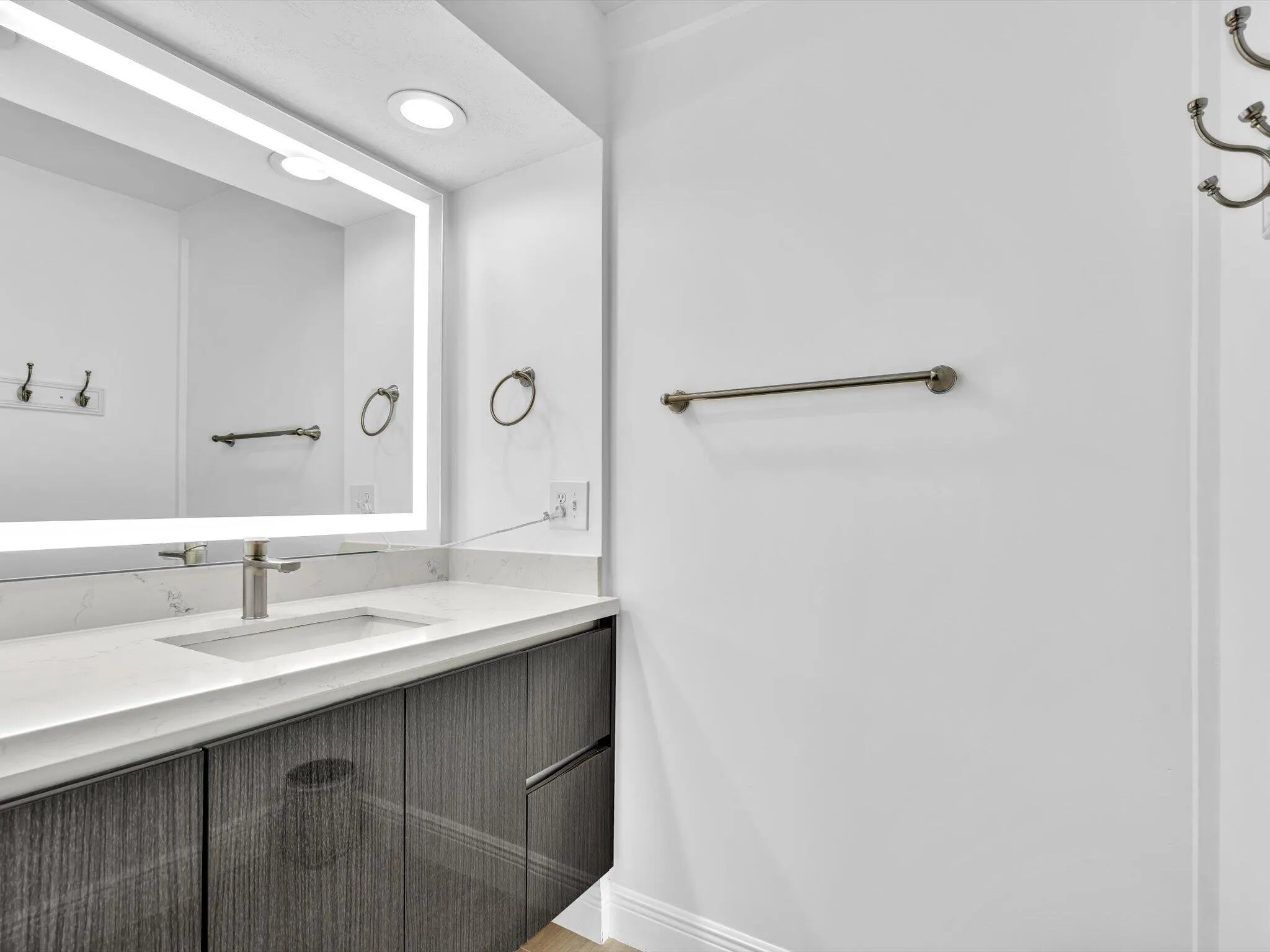 Modern vanity with a light-wood finish, a single integrated sink, a contemporary faucet, and an illuminated mirror