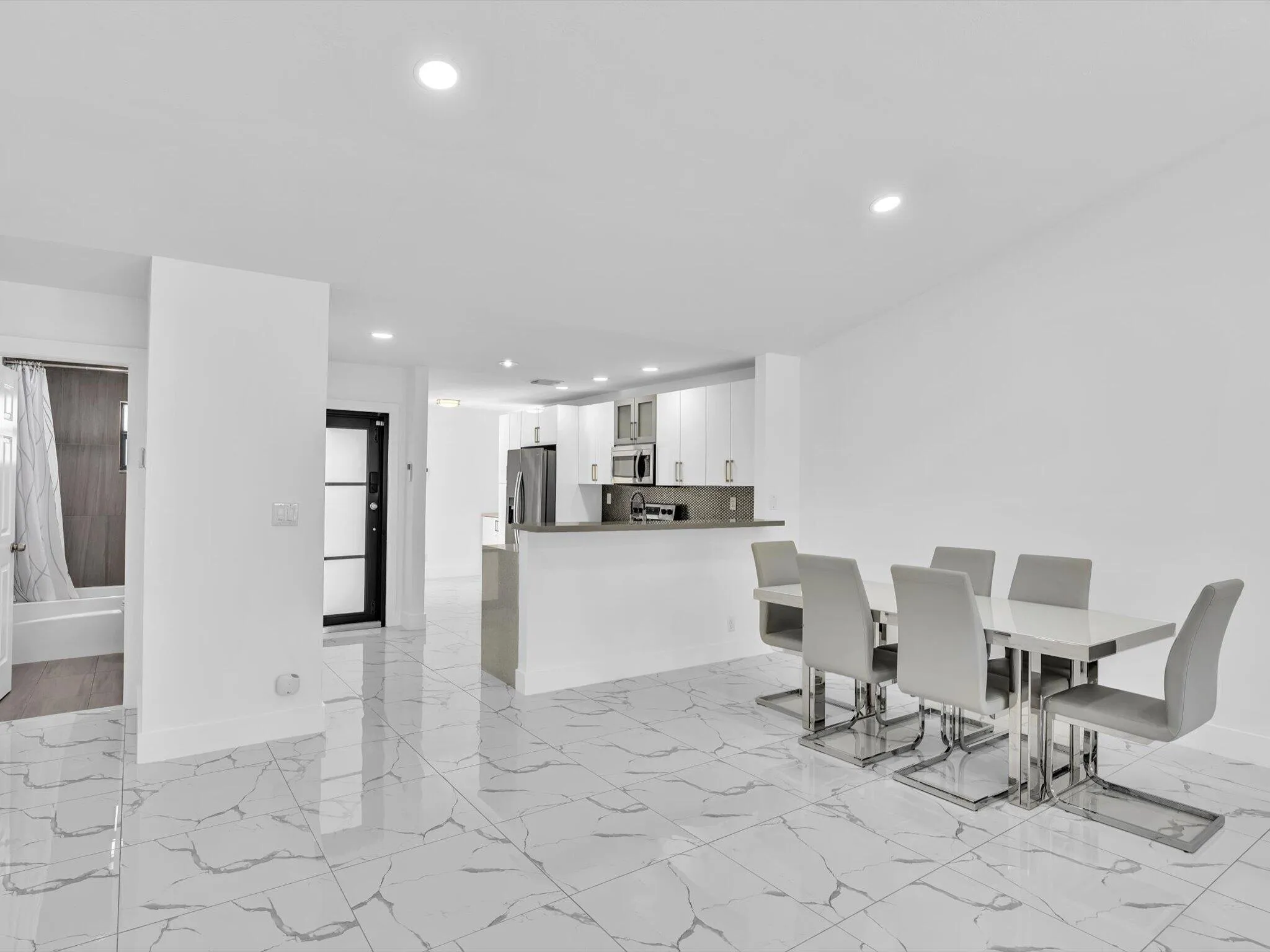Open-concept room with polished tile flooring, recessed lighting, and a modern kitchen featuring stainless steel appliances