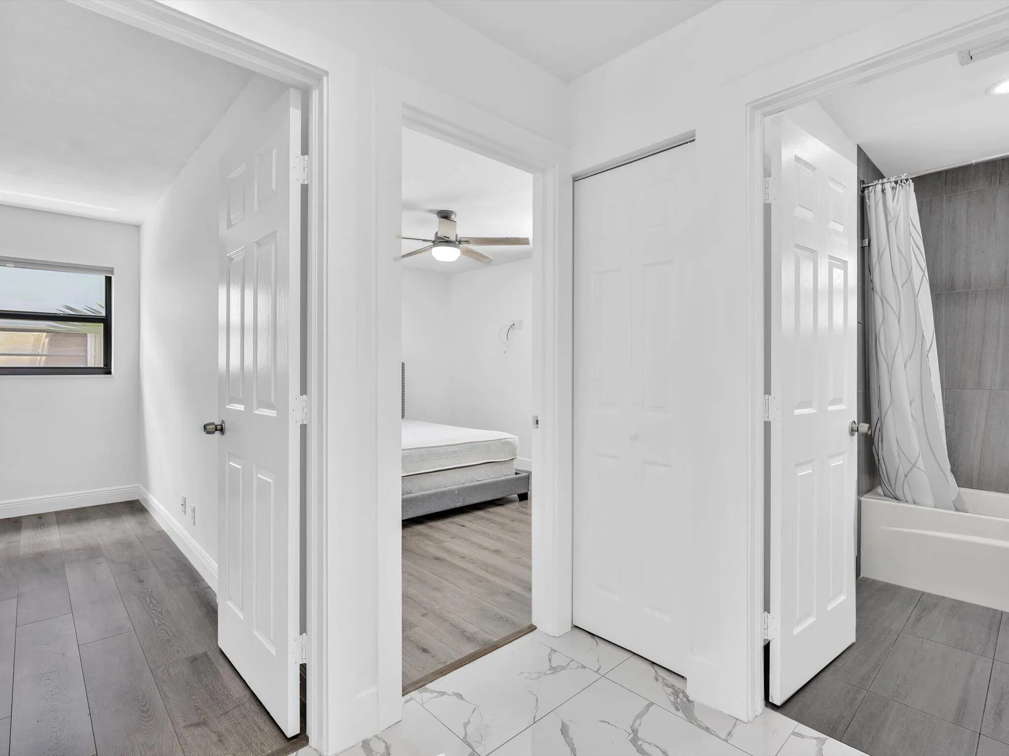 Wood-finish flooring, white panel doors, overhead ceiling fan, white wall finishes, and a white bathtub with dark tile surround