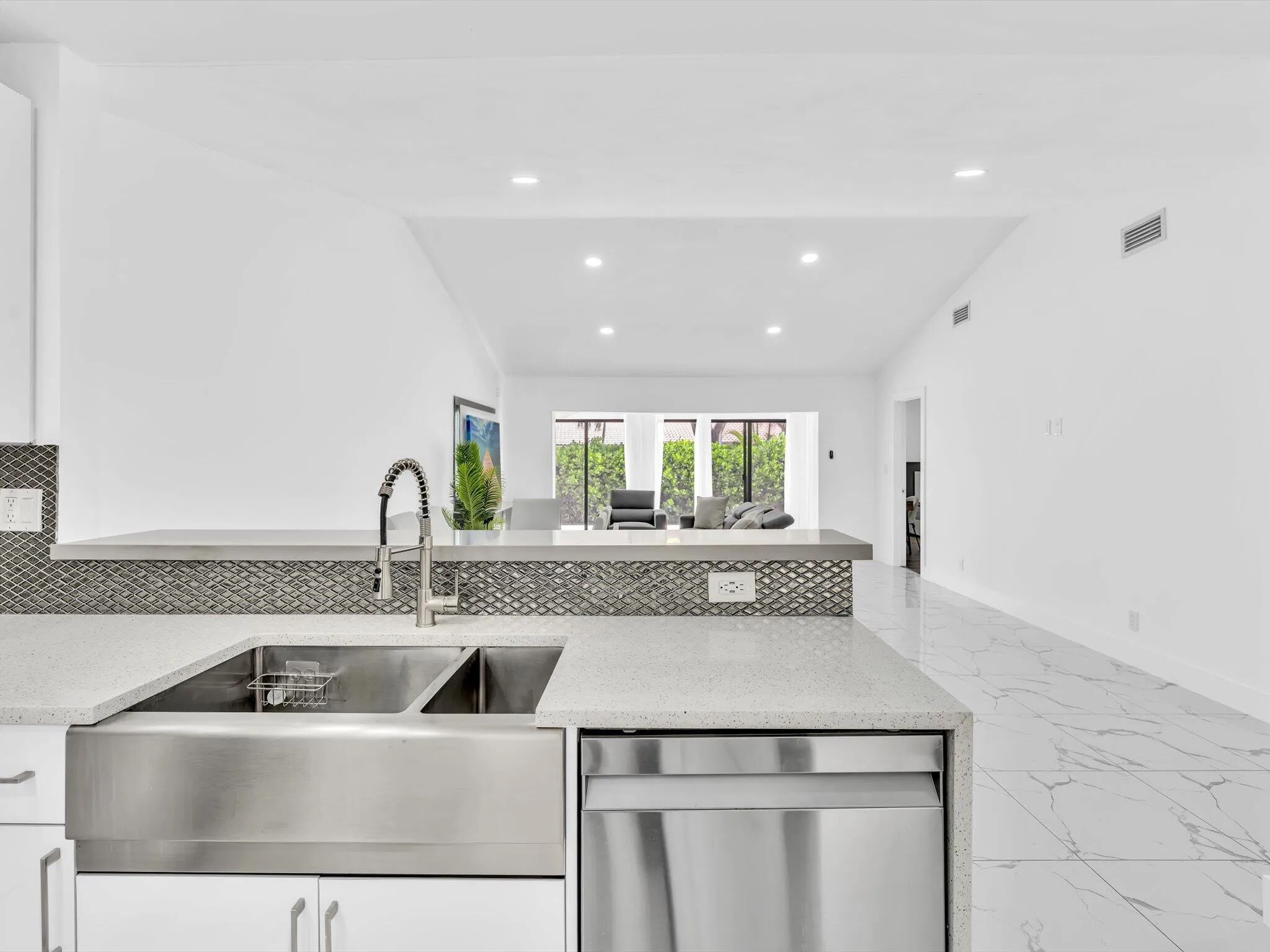 Stainless steel farmhouse sink, integrated dishwasher, light-toned countertops, tile backsplash, recessed lighting