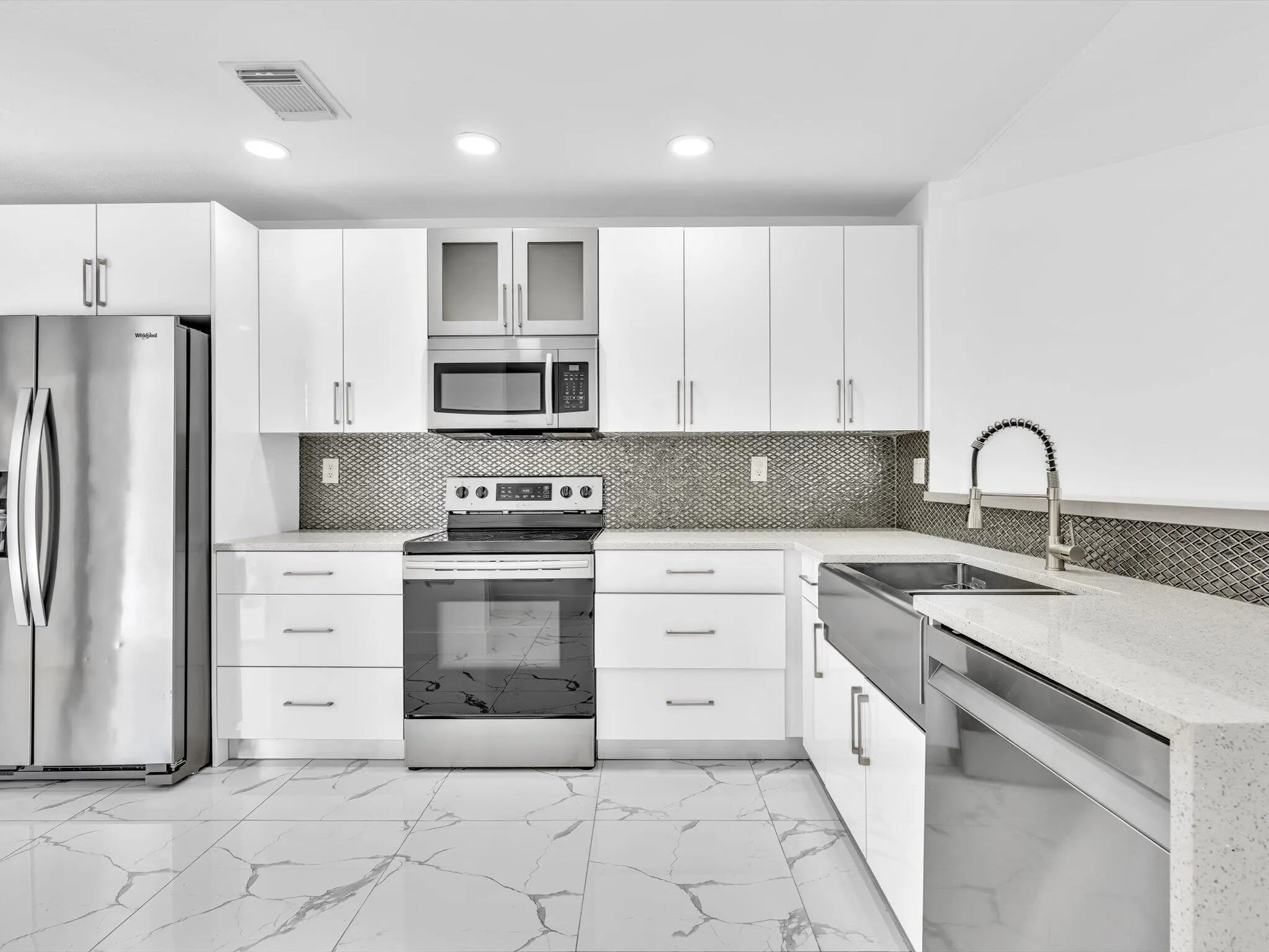 White cabinetry with silver-tone hardware, stainless steel appliances, patterned tile backsplash, light-toned countertops, and large format tile flooring