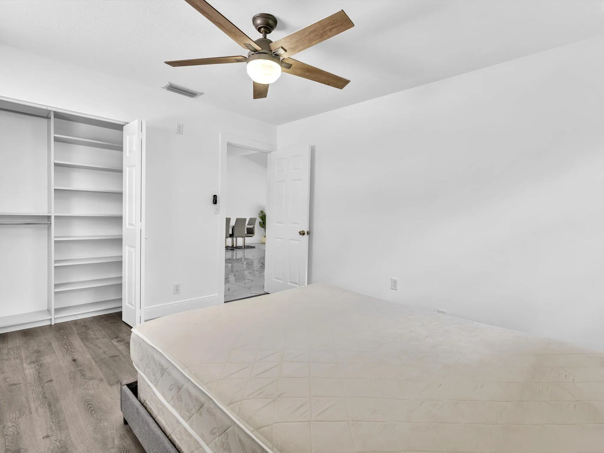 Wood-finish flooring, built-in shelving, ceiling fan with integrated lighting, and white walls