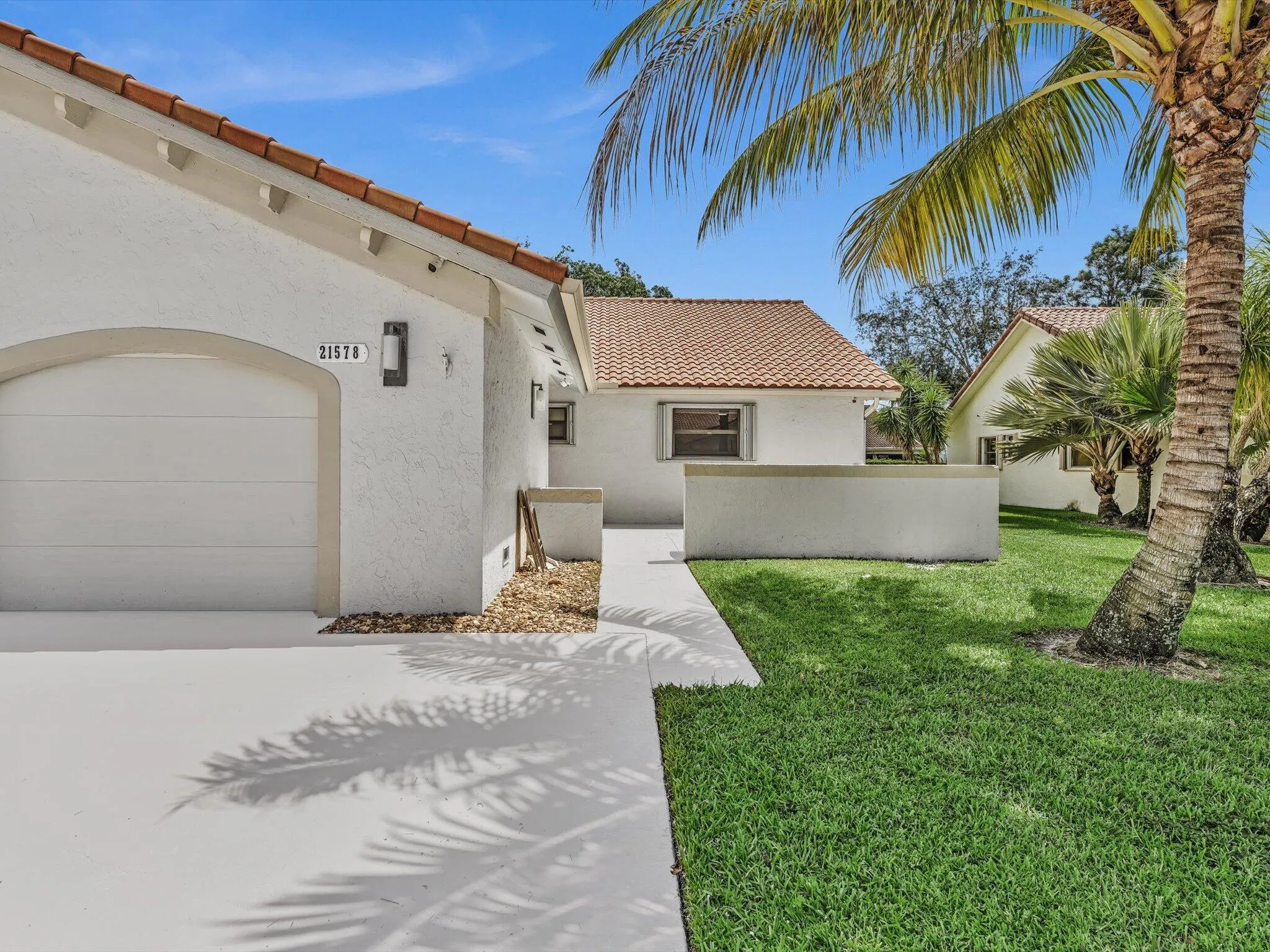 Stucco exterior with a terracotta tile roof, attached garage, manicured lawn, and mature palm trees