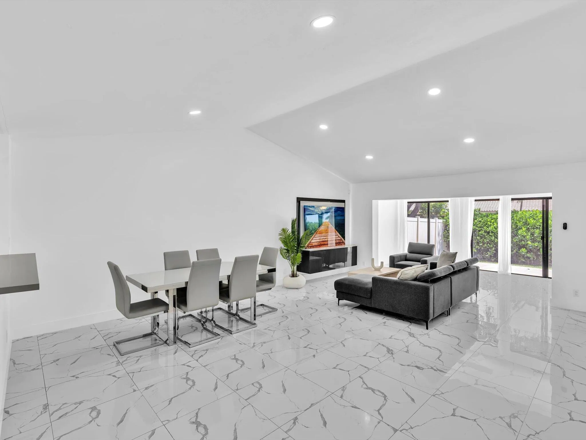 Vaulted ceiling with recessed lighting, large format tile flooring, built-in media console, and glass sliding doors to the exterior