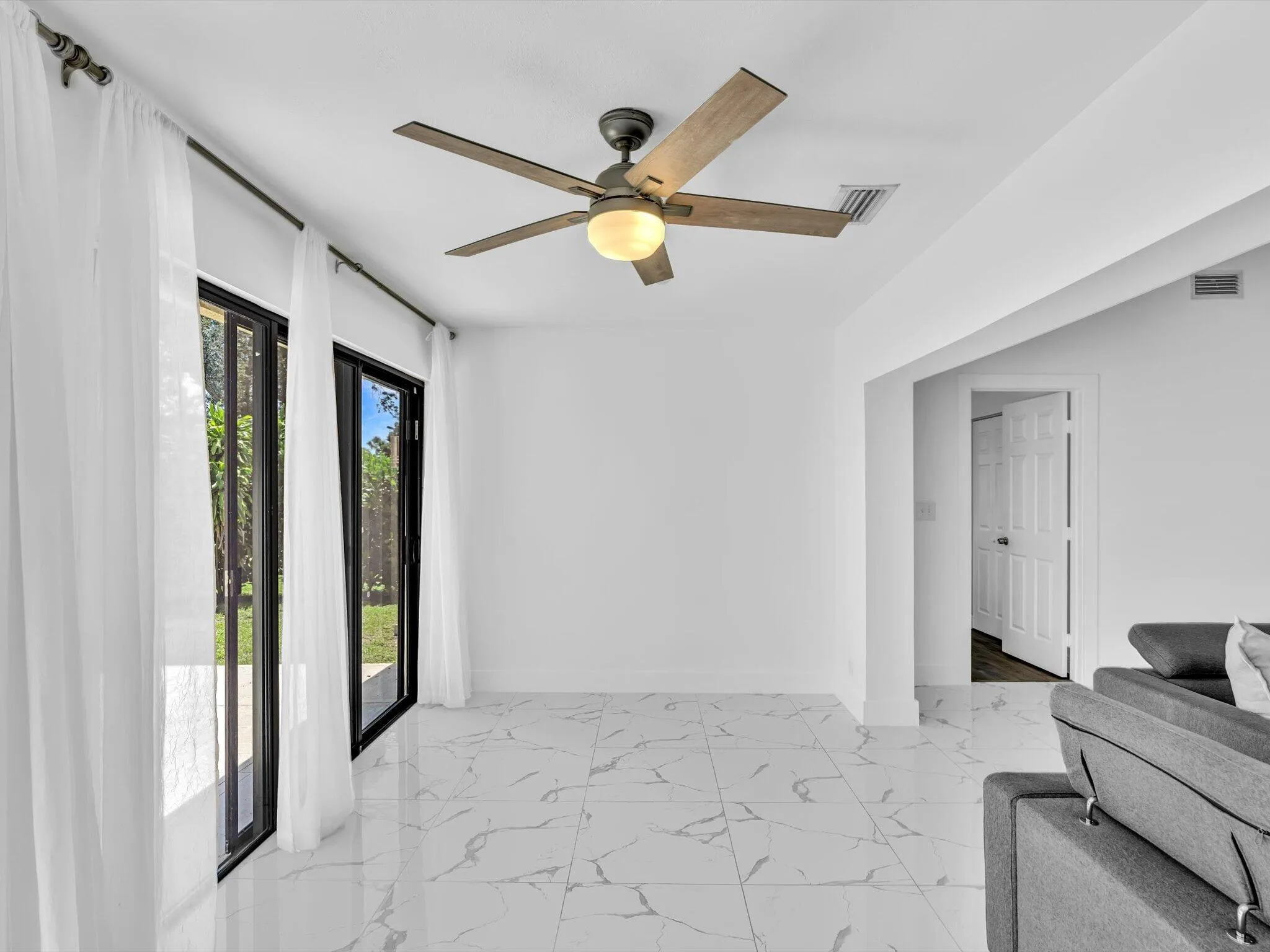 White tile flooring with veining, black-framed sliding glass doors, and a ceiling fan with light fixture