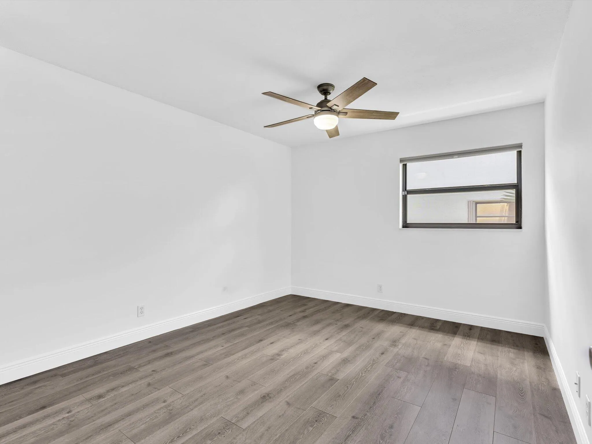 Wood-finish flooring, white painted walls, and a ceiling fan with integrated lighting