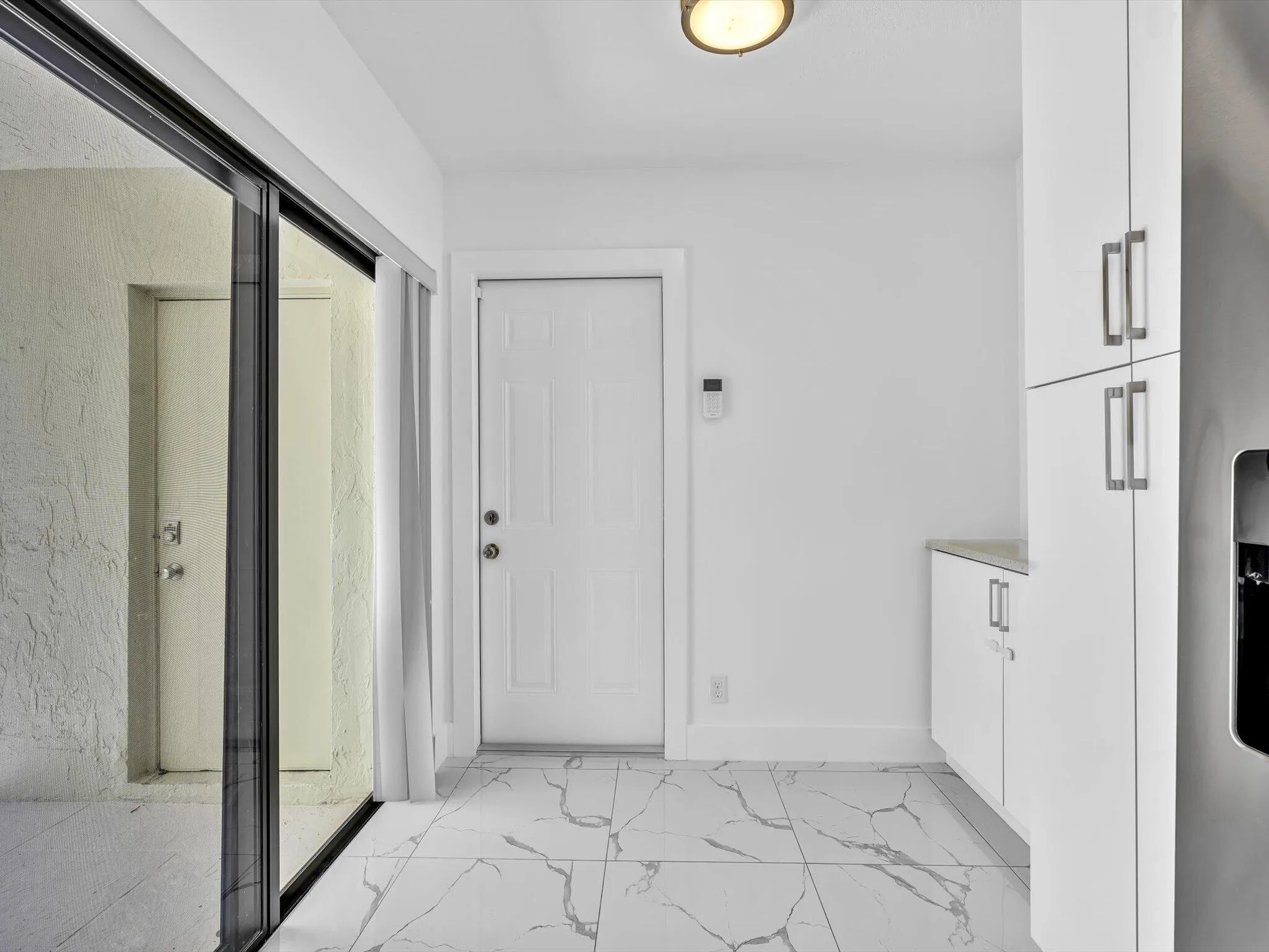 White tiled flooring with grey veining, white cabinetry with silver hardware, sliding glass door, and a white entrance door