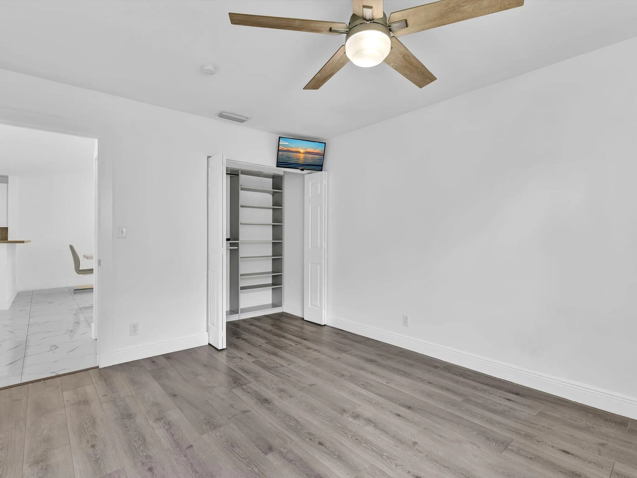 Wood-finish flooring, ceiling fan with integrated lighting, built-in closet shelving, and a clean white wall finish