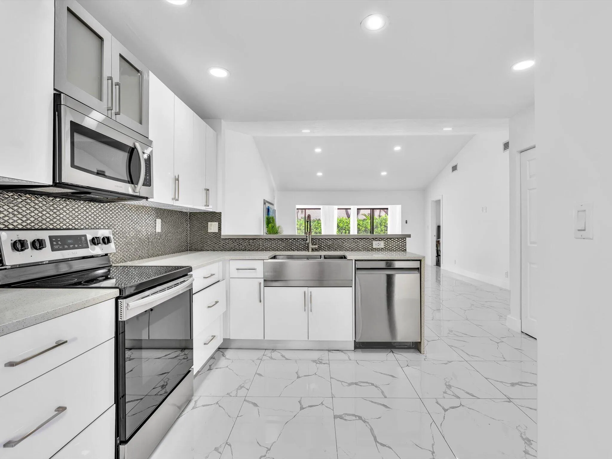 Kitchen featuring white cabinetry, stainless steel appliances, a tile backsplash, light-toned countertops, and large format flooring