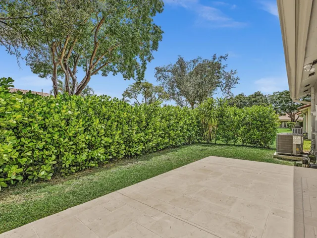 Expansive patio with stone-finish pavers, surrounded by lush green lawn and mature privacy hedges