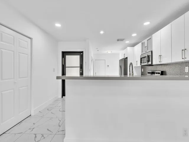 Contemporary kitchen with white cabinetry, stainless steel appliances, a mosaic tile backsplash, and a breakfast bar