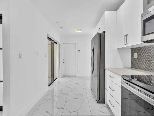 Kitchen featuring white cabinetry, stainless steel appliances, a tile backsplash, light-toned countertops, and tile flooring