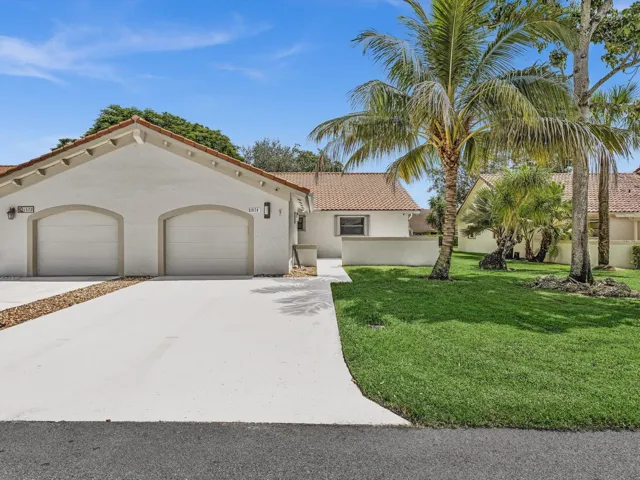 Stucco exterior with a tile roof, two-car garage, concrete driveway, and established palm trees