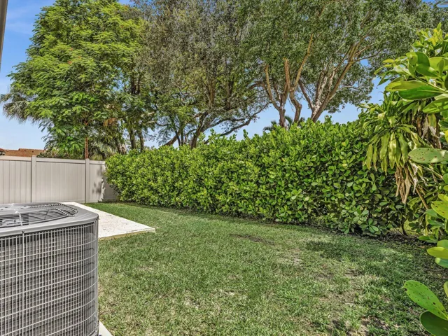 Landscaped backyard featuring a grass lawn, mature trees, and a privacy hedge