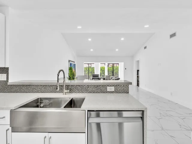 Stainless steel farmhouse sink, integrated dishwasher, light-toned countertops, tile backsplash, recessed lighting