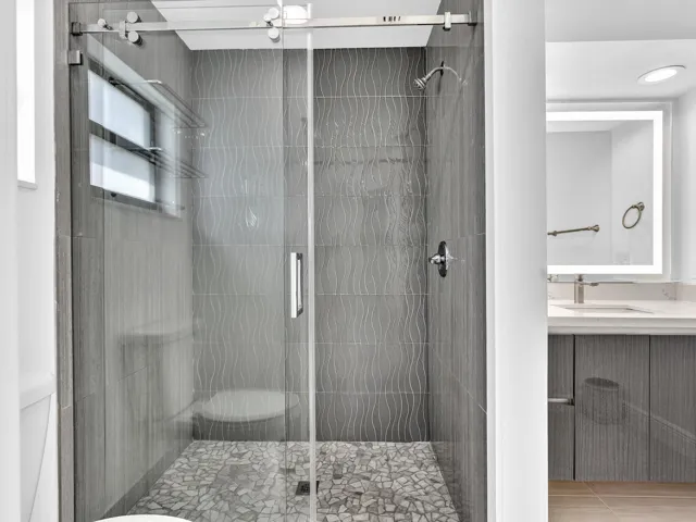 Glass-enclosed shower with pebble-style flooring, textured wall tile, and a built-in shower bench