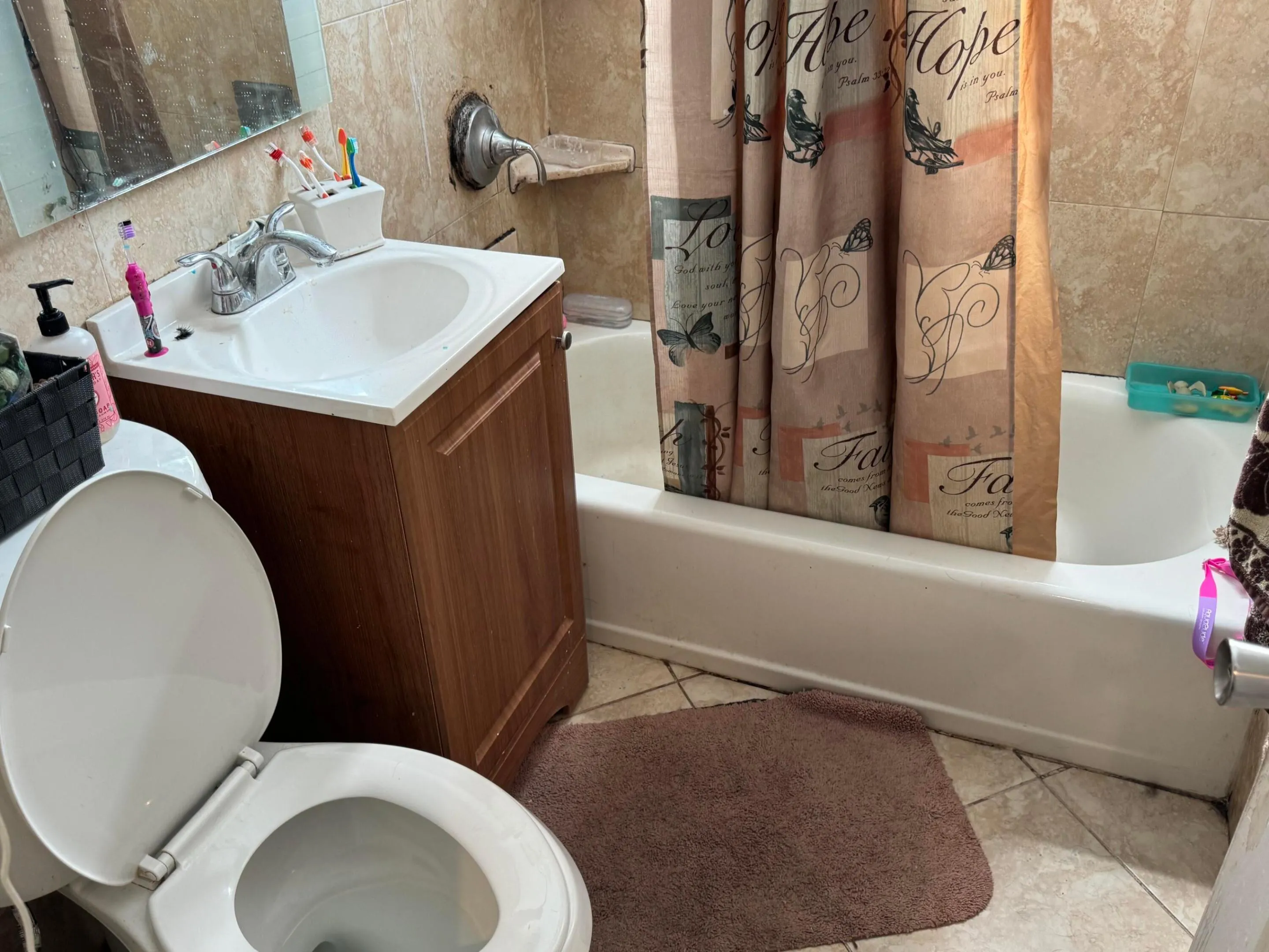 Bathroom featuring a white toilet, wood-finish vanity with an integrated sink, tiled walls, and a bathtub with a shower fixture