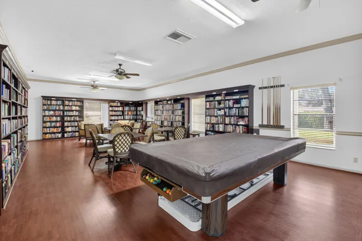 Wood-finish flooring throughout, featuring a billiards table, built-in library shelving, and ceiling fans