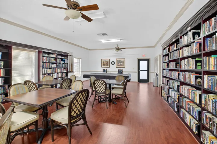 Community library featuring extensive built-in shelving, wood-finish flooring, ceiling fans, and a billiards table